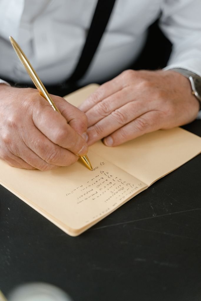 Man's hands writing in a notebook with a gold pen. Close-up view of writing process.