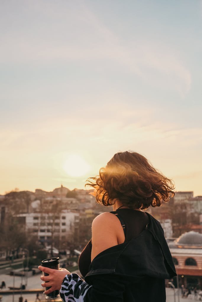 Woman holding coffee cup and enjoying city sunrise view.